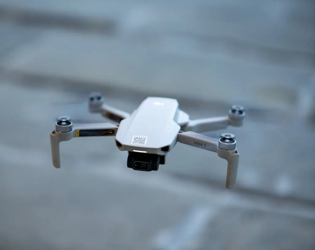 A small white drone flying over a brick wall
