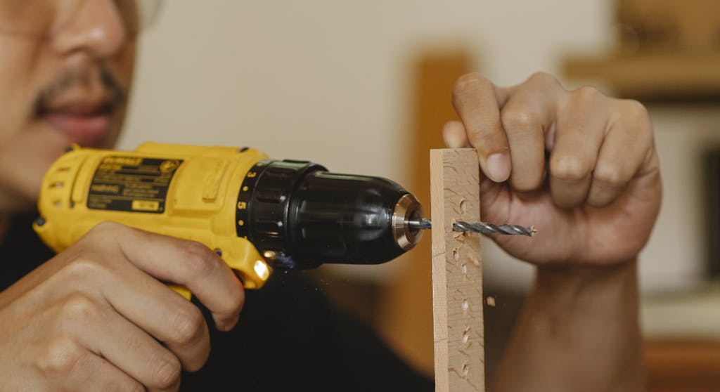 Crop man drilling holes in wooden plank