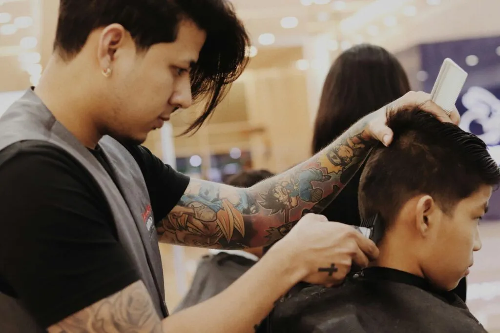 Tattooed barber styles young boy's hair in modern salon setting.