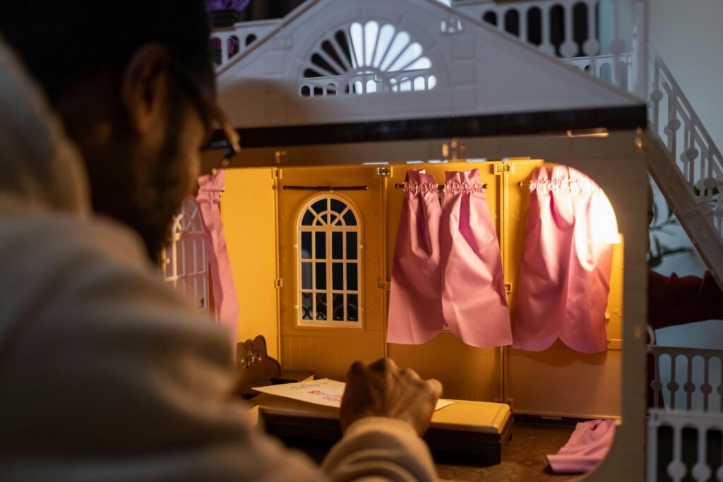 A person arranging miniature furniture inside a dollhouse, focused on interior lighting details.
