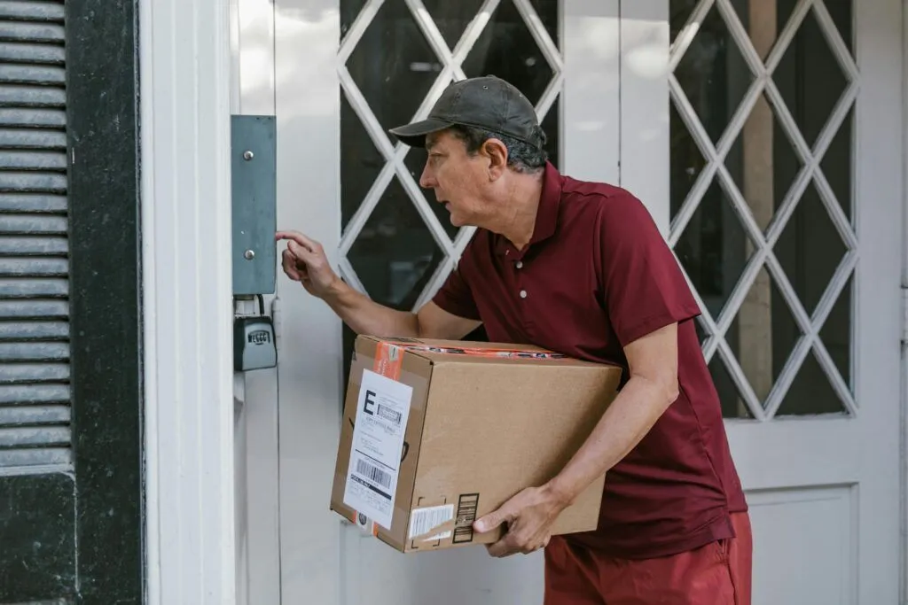 Man delivering a package at a front door, wearing a red shirt and cap.