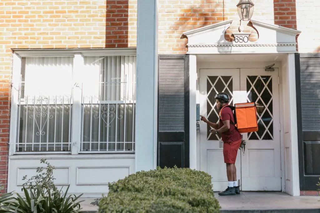 Delivery person pressing doorbell with package at a house entryway, showcasing modern logistics.