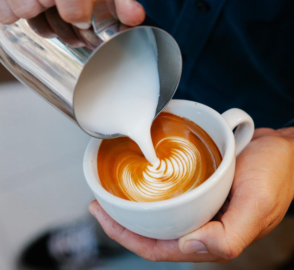 Crop unrecognizable male cafe worker pouring fresh milk from pitcher into aromatic coffee with foam