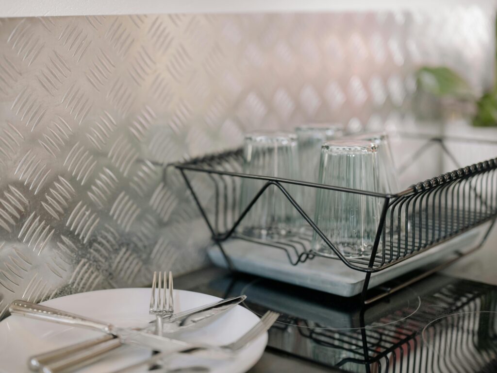 Close-up of a kitchen dish rack with glassware and utensils on a clean countertop.