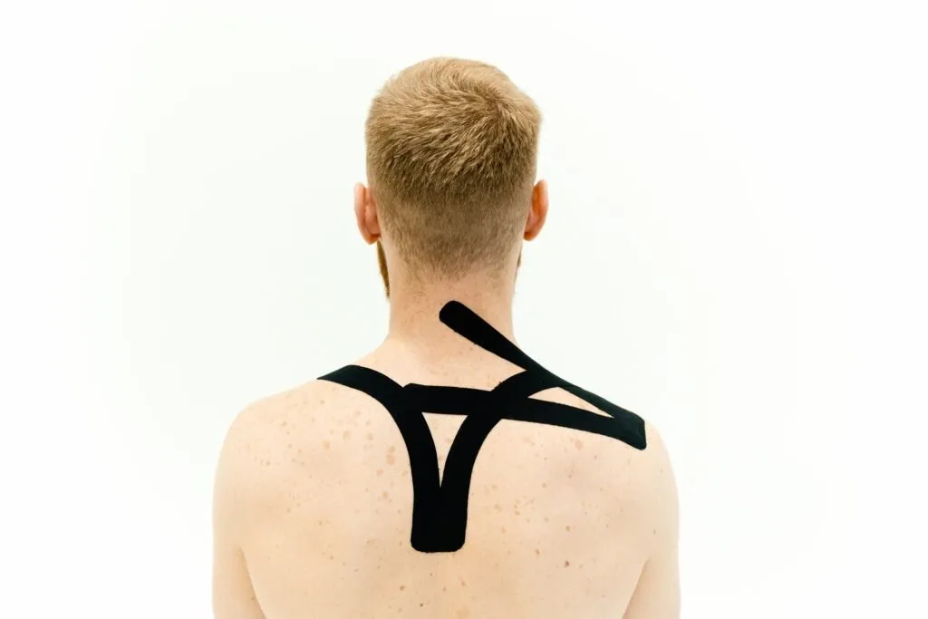 A man with kinesiology tape applied on shoulders. Back view against white background.