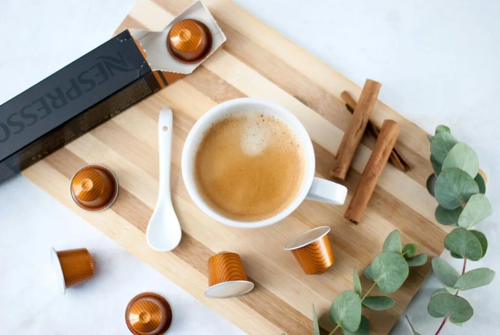 Elegant coffee setup with Nespresso capsules, cinnamon, and eucalyptus, perfect for a stylish coffee break.