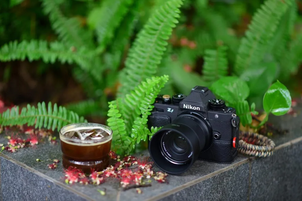 Close-up of a Nikon camera and coffee glass on a garden ledge with lush greenery.