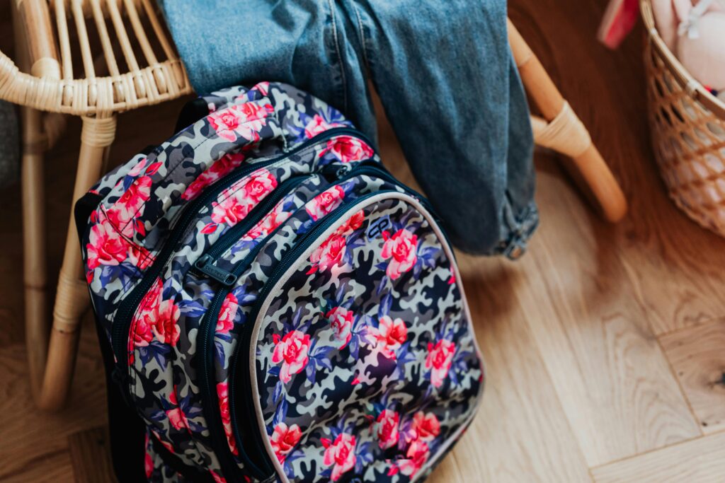 Vibrant floral patterned backpack on a wooden floor beside wooden furniture.