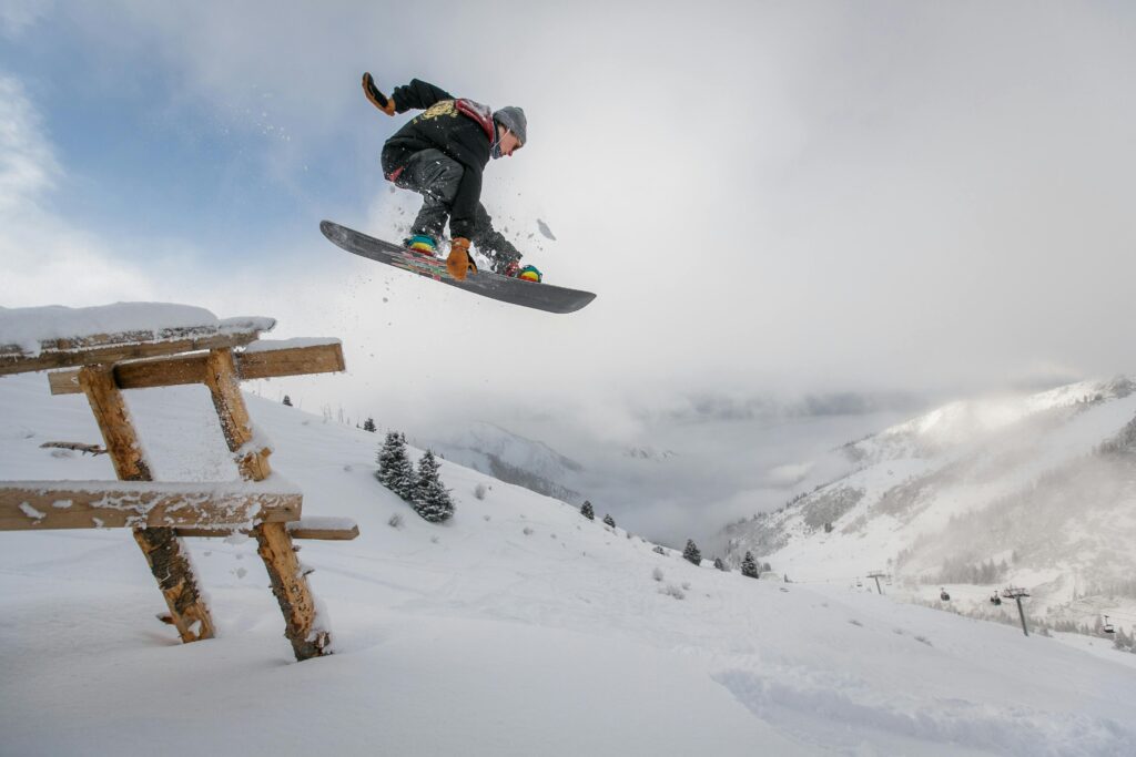Snowboarder executing a jump over a snowy bench in a scenic winter mountain setting.