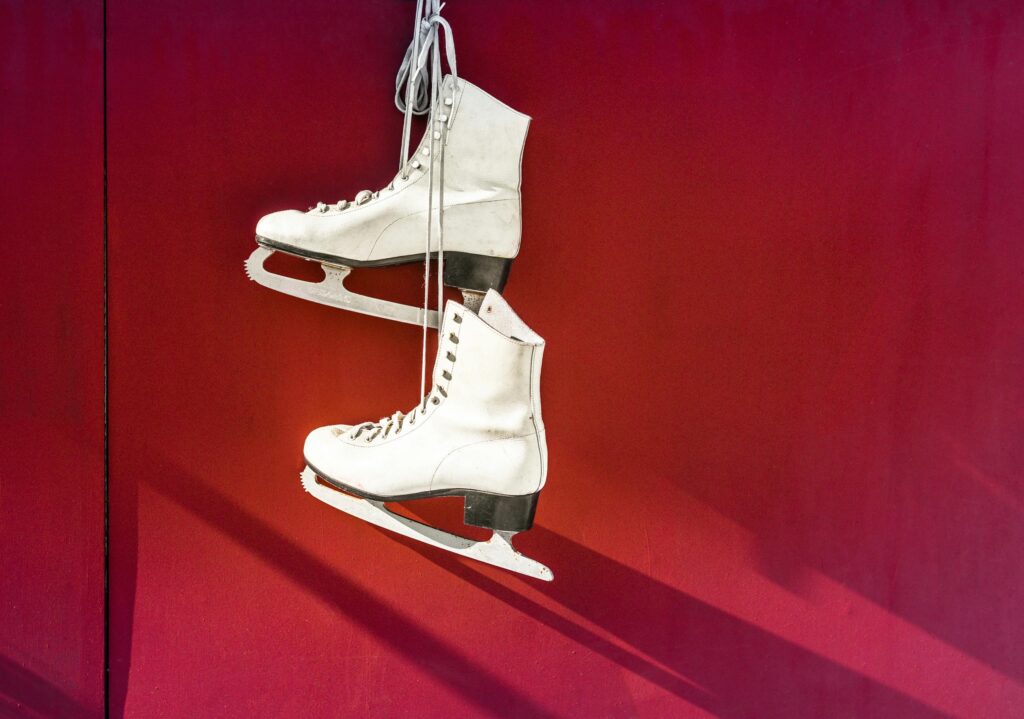 Pair of white ice skates hanging on a vibrant red wall, perfect for winter sports imagery.